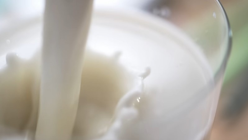 Fresh milk is poured into a clear glass, creating ripples and splashes
