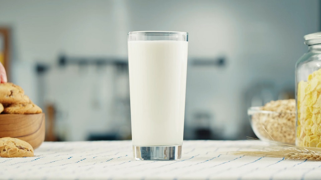 Čaša mleka na stolu, u pozadini činija sa keksom i tegla žitarica