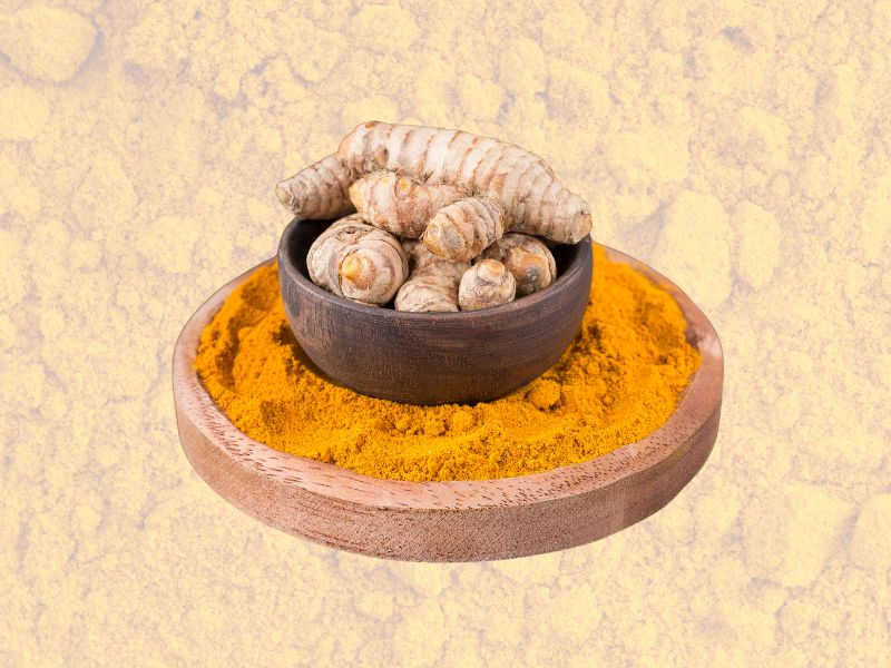 Drvena posuda sa svežim korenom kurkume položena na sloj kurkume u prahu na svetloj pozadini